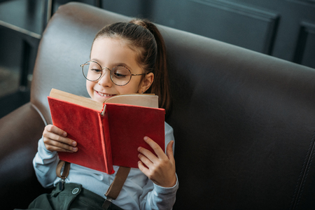 happy little child reading book on couch at homeの写真素材