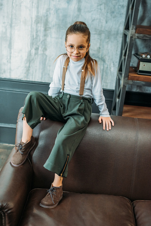 adorable little child in stylish clothing sitting on couch in loft apartmentsの写真素材