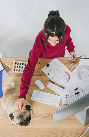 Young woman cuddling pug dog while working on designs by tableの写真素材