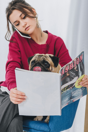 Attractive young girl talking on the phone and hugging pug dogの写真素材