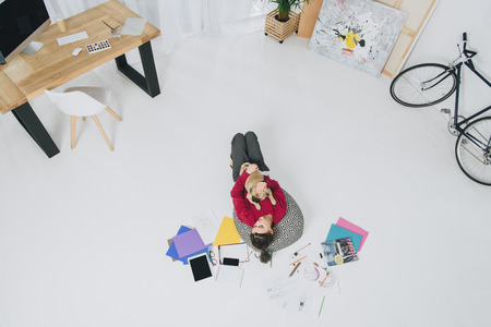 Young woman playing with pet dog of floor of home officeの写真素材