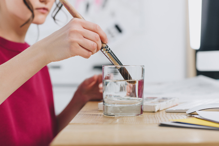 Cropped view of female illustrator cleaning brush in glassの写真素材