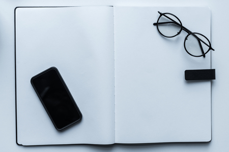 top view of smartphone and glasses on open notebookの写真素材