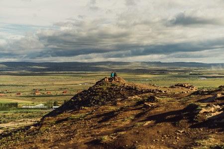 back view of couple sitting on cliff and looking at scenic wild landscape in Icelandの写真素材