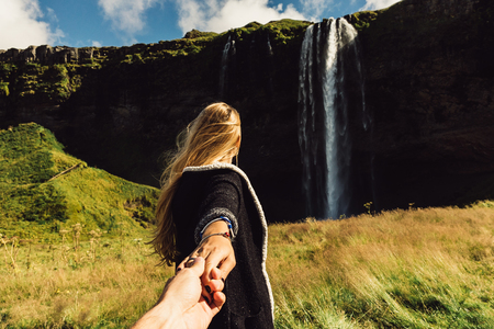 cropped shot of girl holding hand of friend and going to majestic waterfall in Icelandの写真素材