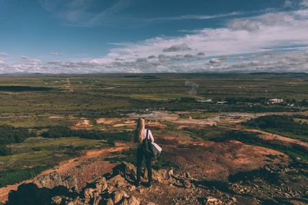back view of young woman standing on cliff and looking at majestic landscape in Icelandの写真素材