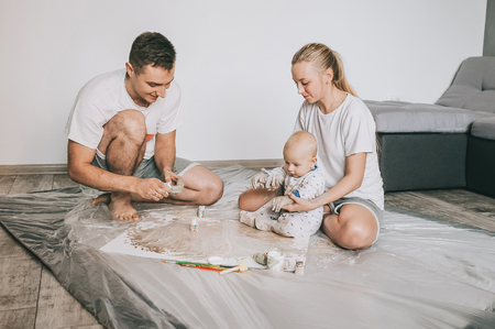 beautiful happy young family with infant child painting together on floorの写真素材