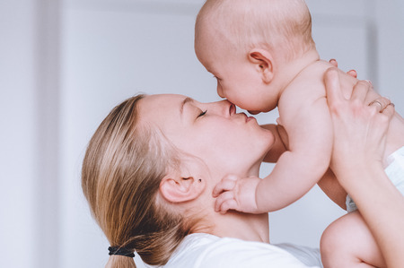 young loving mother carrying and kissing her infant childの写真素材