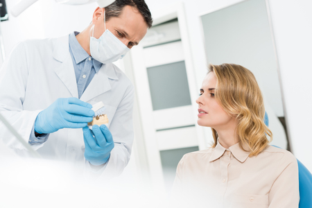 Doctor showing jaws model to female patient in modern dental clinicの写真素材