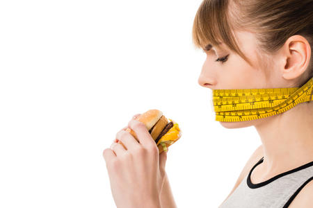 woman with mouth tied in measuring tape trying to eat burger isolated on whiteの写真素材