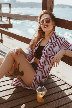 attractive young woman sitting on floor of pier at beachの写真素材
