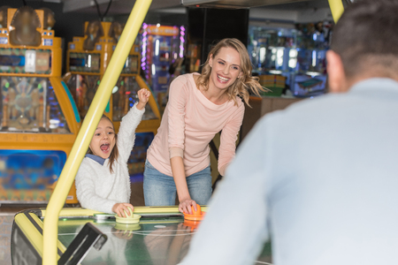 selective focus of parents with happy little daughter playing air hockey in game centerの写真素材