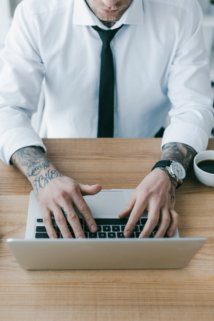 cropped shot of businessman with tattoos using laptop at workplaceの写真素材