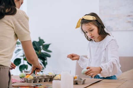 concentrated little daughter painting easter eggs together with motherの写真素材
