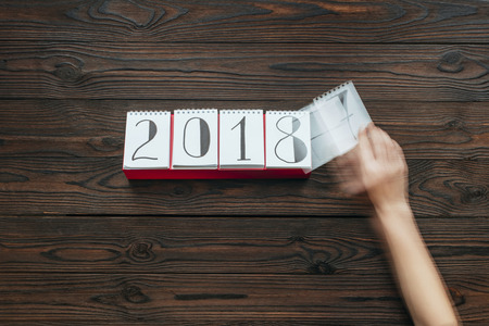 cropped shot of woman tearing calendar paper of 2018 year with dark wooden surface as backgroundの写真素材