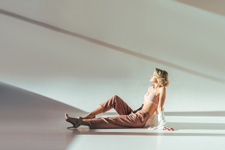 full length view of beautiful sensual woman in pink bra and high heeled shoes sitting on greyの写真素材