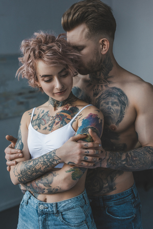 tender tattooed couple embracing in bedroom at homeの写真素材