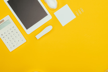 top view of digital tablet with blank screen, calculator and office supplies isolated on yellowの写真素材