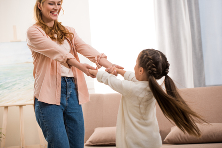 beautiful happy mother and daughter holding hands and smiling each other at homeの写真素材