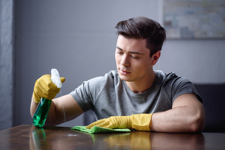 man cleaning table in living room with spray bottle and ragの写真素材