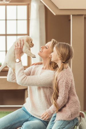 mother and little daughter playing with adorable labrador puppyの写真素材
