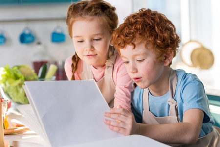 focused little kids reading cookbook while cooking together in kitchenの写真素材