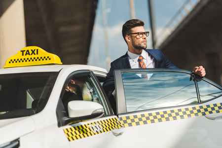 hansome young man in suit and eyeglasses looking away while sitting in taxi cabの写真素材
