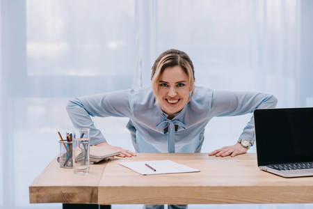 happy businesswoman doing push up on table at officeの写真素材