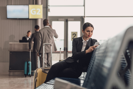 young businesswoman waiting for plane at airport lobby and using smartphoneの写真素材