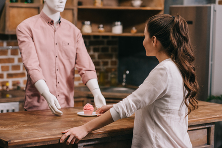 selective focus of woman giving cupcake to manikin in casual clothing, loneliness conceptの写真素材