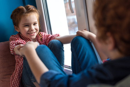 selective focus of cute little kids holding hands and smiling each other while sitting on windowsillの写真素材