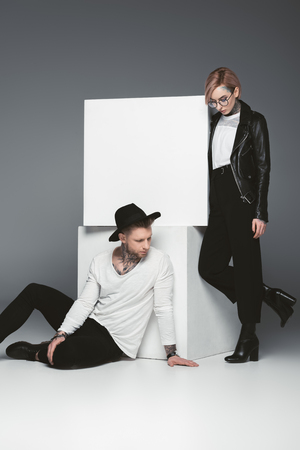 stylish tattooed couple posing near white cubes, isolated on greyの写真素材