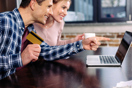 happy couple with credit card and cup of coffee looking at laptop screen at homeの写真素材
