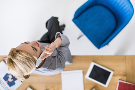 overhead view of businesswoman talking on smartphone at workplace in officeの写真素材