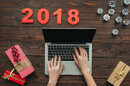 cropped shot of woman typing on laptop with 2018 numbers and wrapped gifts on wooden tabletopの写真素材
