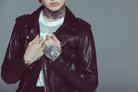 cropped view of tattooed girl in black leather jacket, isolated on greyの写真素材