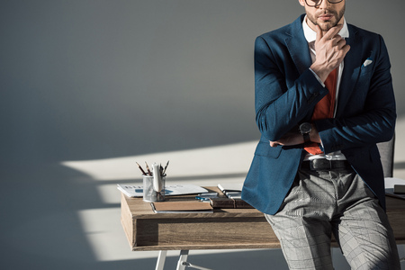 cropped shot of stylish young businessman with hand in chin sitting on tableの写真素材