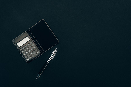 top view of calculator and pen on black background