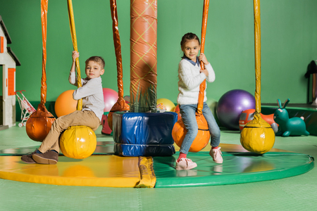 cute happy little kids looking at camera while swinging in entertainment centerの写真素材
