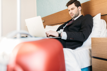 businessman lying on bed in hotel room and using laptopの写真素材