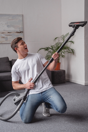 handsome man having fun with vacuum cleaner in living roomの写真素材