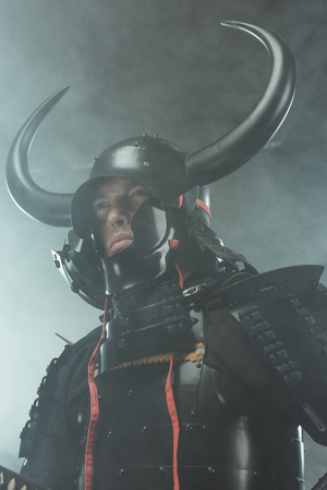 bottom view of samurai in traditional armor on dark background with smokeの写真素材