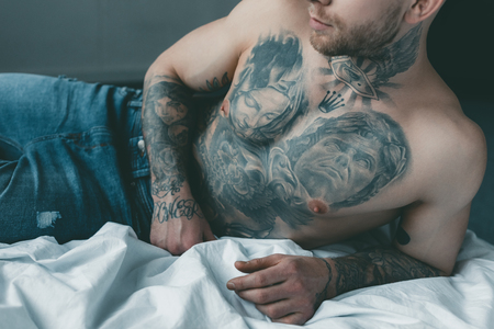 cropped view of shirtless tattooed man lying on bedの写真素材