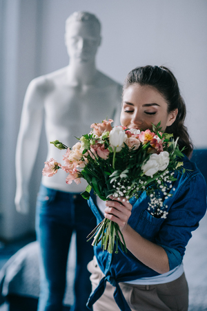 selective focus of young woman with bouquet of flowers and mannequin behind, one way love conceptの写真素材