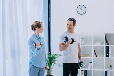 attractive businesswoman and her personal trainer working out with dumbbells at officeの写真素材