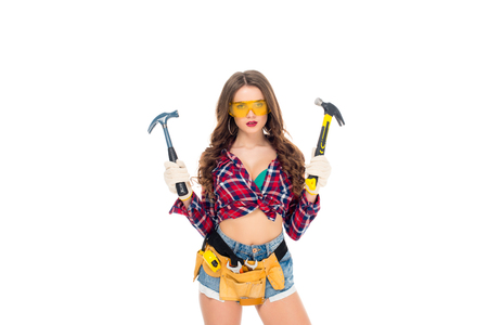 beautiful girl in goggles and gloves with tool belt holding hammers, isolated on whiteの写真素材