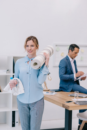 businesswoman with fitness equipment standing at modern office while her colleague working blurred on backgroundの写真素材
