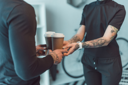 cropped shot of coworkers holding paper cups with coffee to goの写真素材