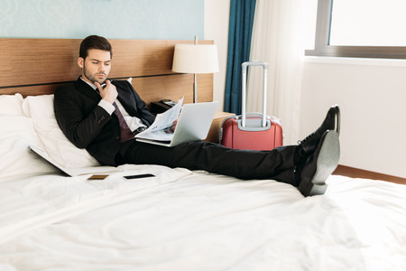 businessman lying on bed in hotel room and reading newspaperの写真素材