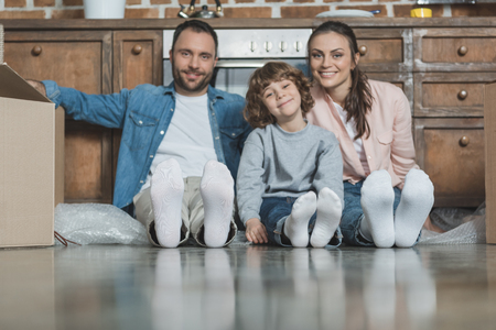 happy family with one child smiling at camera while sitting on floor during relocationの写真素材